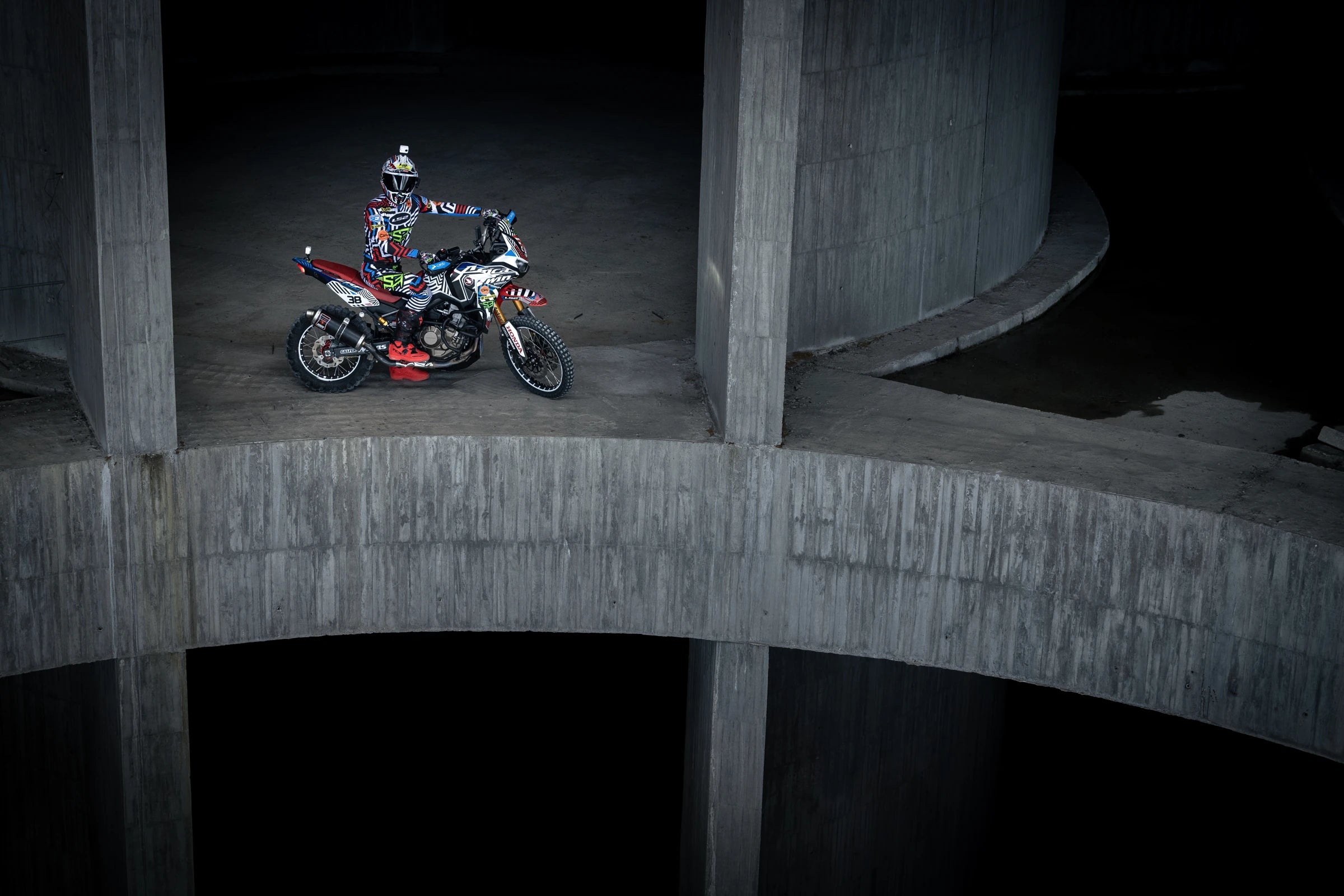 Piloto sobre una Honda Africa Twin con gráficos Uniracing en una estructura de hormigón